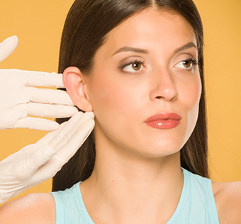 Γυναίκα κοντινό μετά από ωτοπλστική. Δύο χέρια γιατρού δείχνουν το αυτί της.