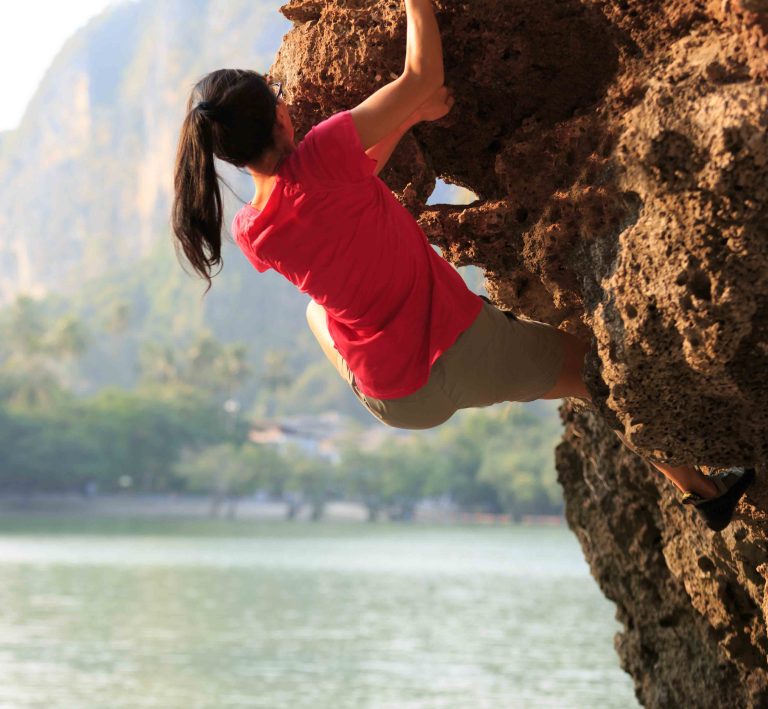 Γυναίκα κάνει αναρρίχηση σε βράχο δίπλα στη θάλασσα