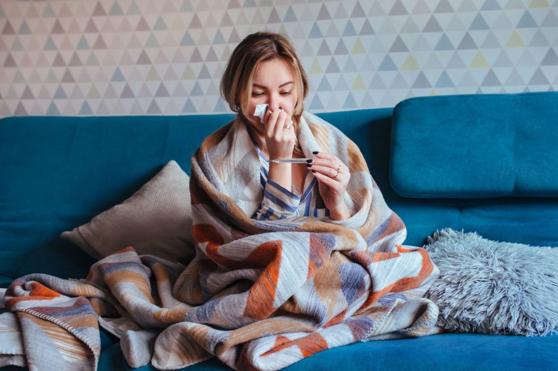 άρρωστη γυναίκα κάθεται σκεπασμένη στον καναπέ
