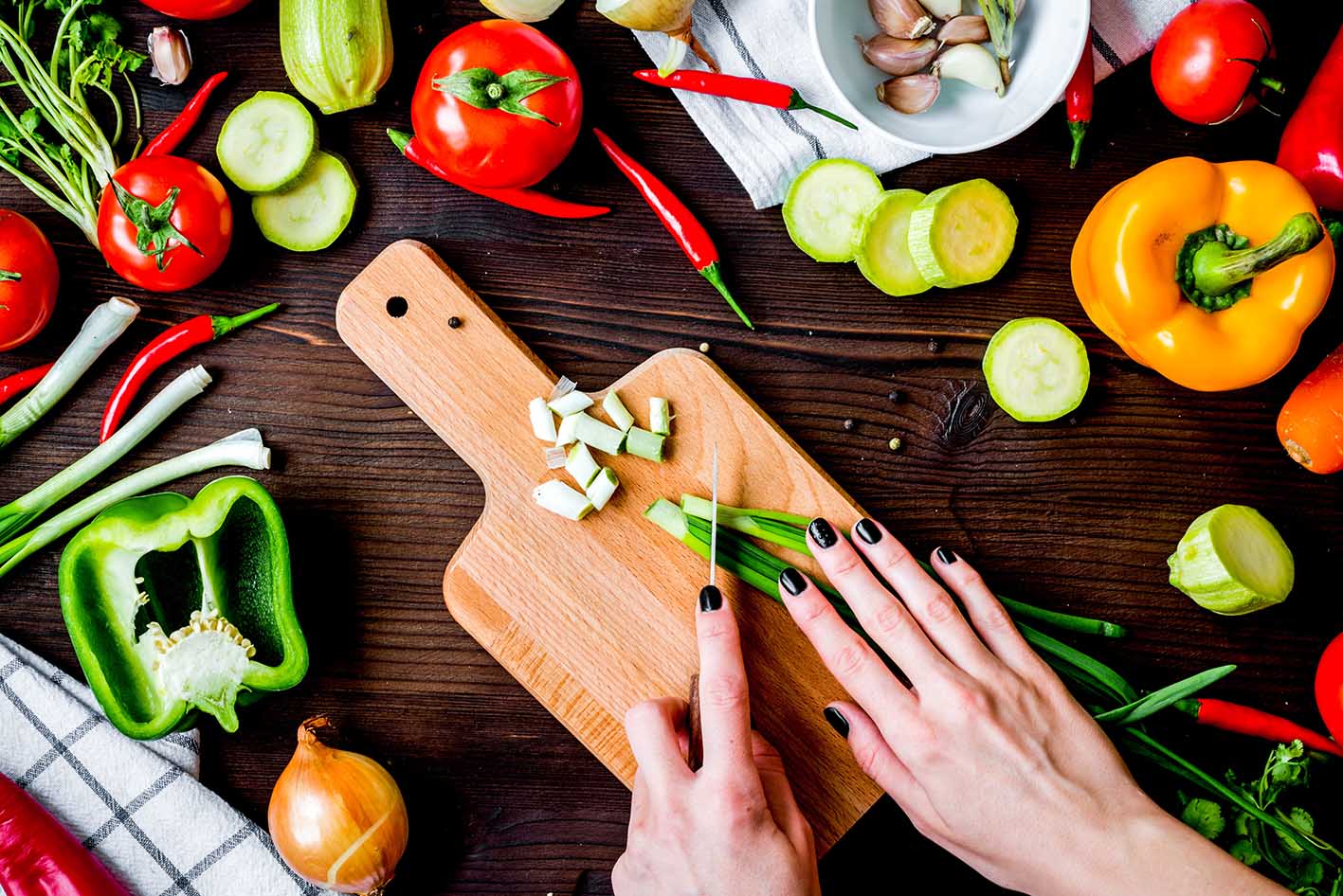 Χέρια κόβουν πάνω στον ξύλινο πάγκο λαχανικά