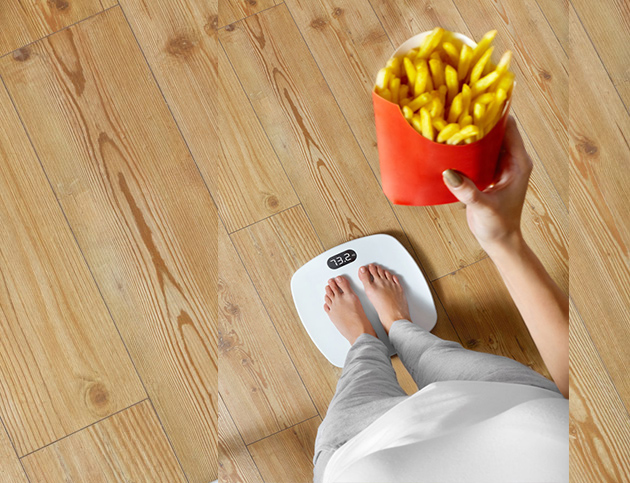 Γυναίκα στη ζυγαριά με fast food τροφή στα χέρια της