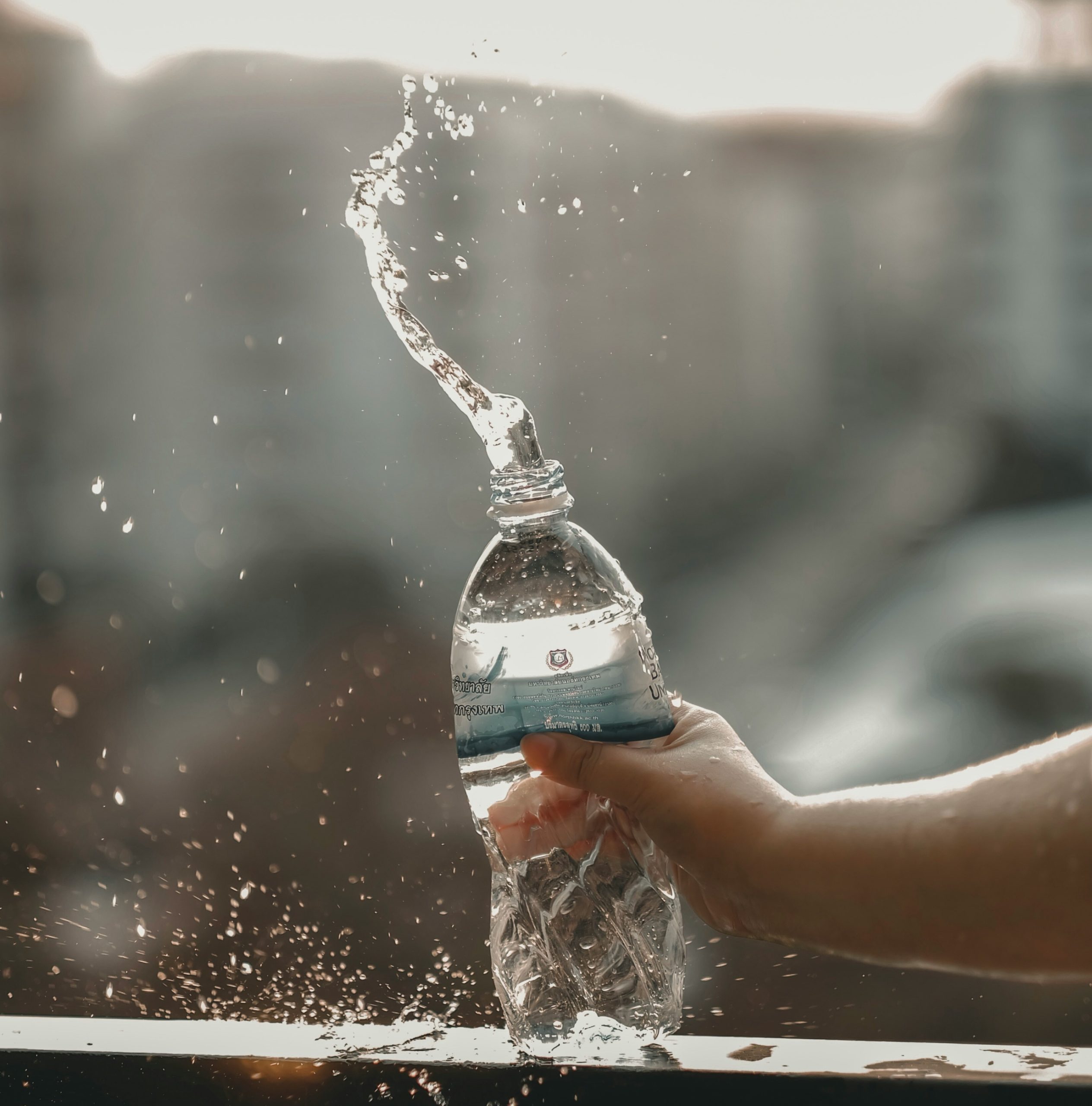 ένα χέρι πιέζει μικρό πλαστικό μπουκάλι νερό και πετιέται το νερό