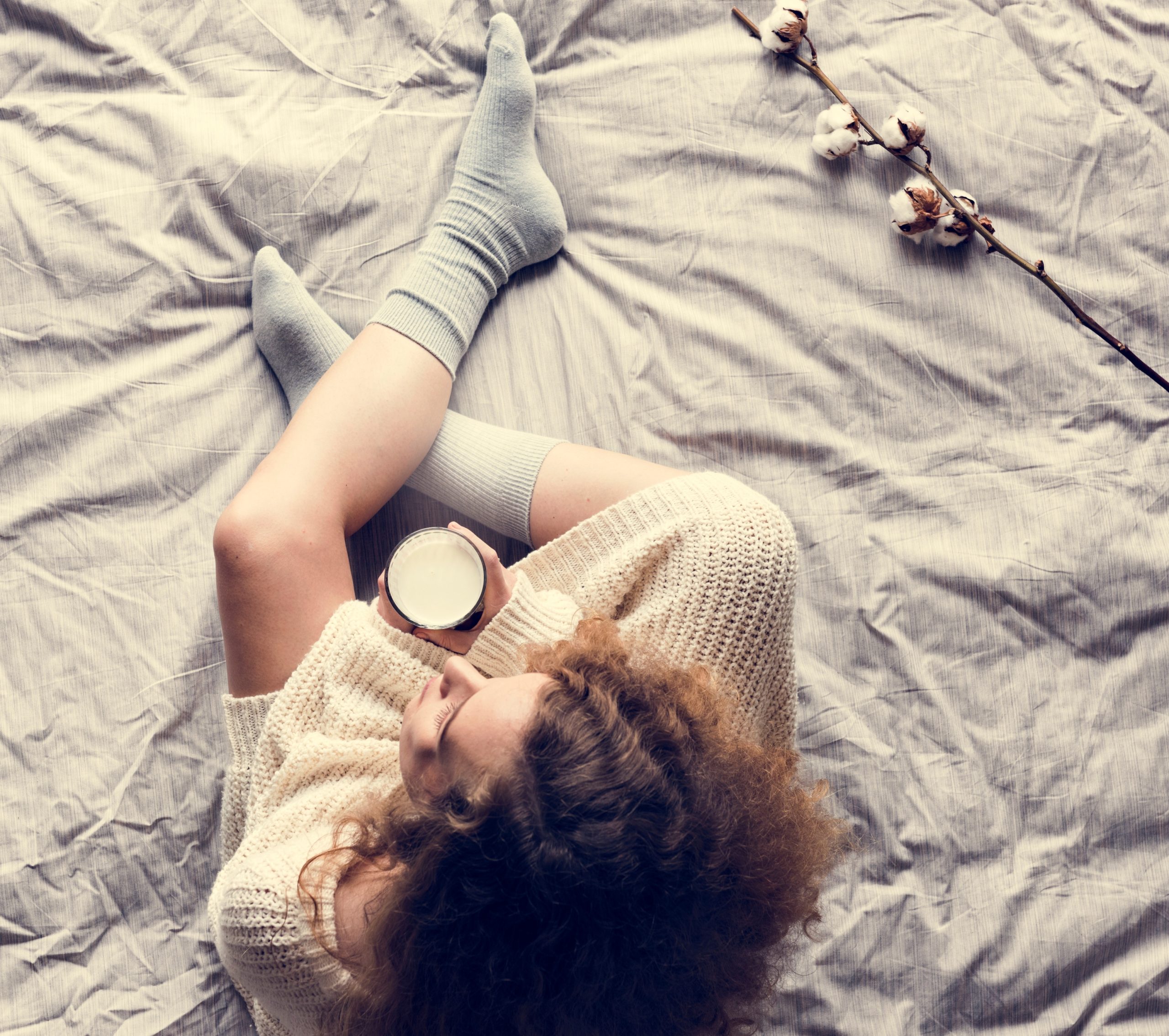 γυναίκα κάθεται στο κρεβάτι και κρατά ένα φλιτζάνι ζεστό γάλα