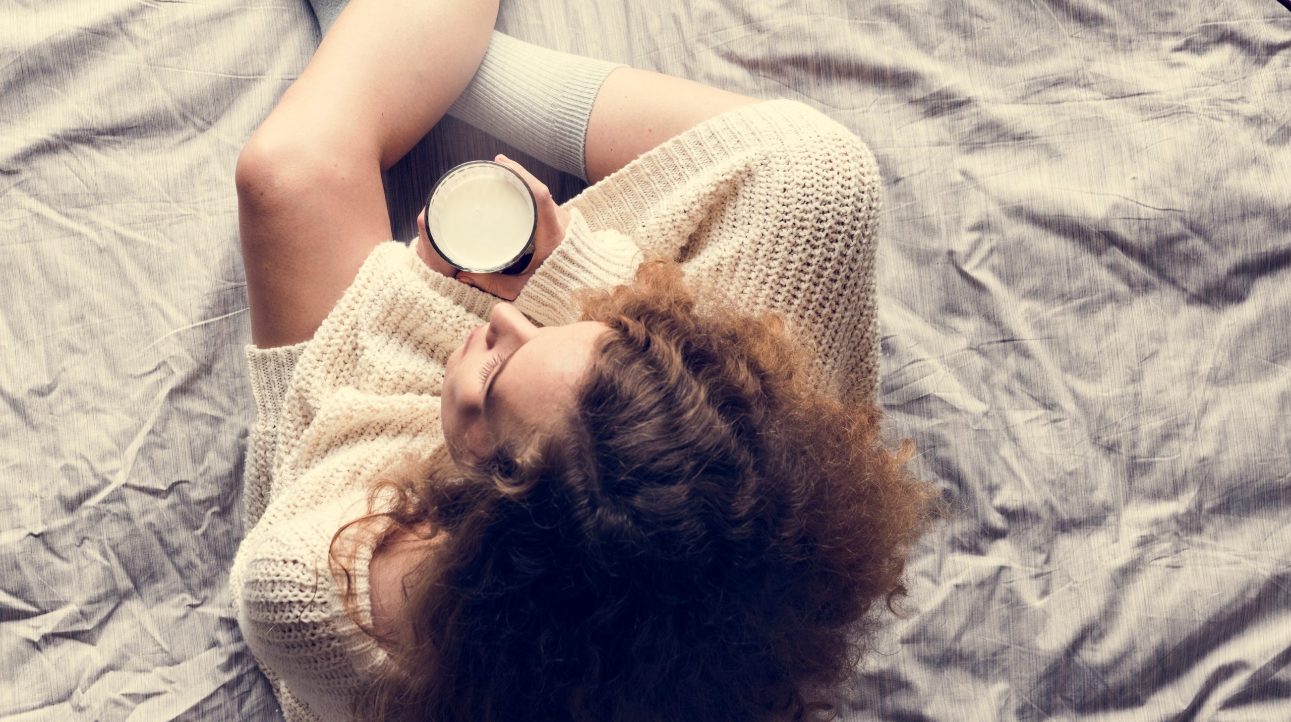 γυναίκα κάθεται στο κρεβάτι και κρατά ένα φλιτζάνι ζεστό γάλα