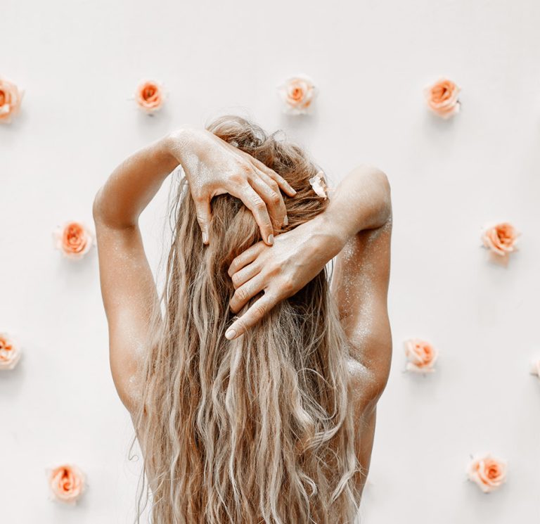 Γυναίκα με μακριά μαλλιά μας γυρνά την πλάτη της - τριαντάφυλλα στον τοίχο