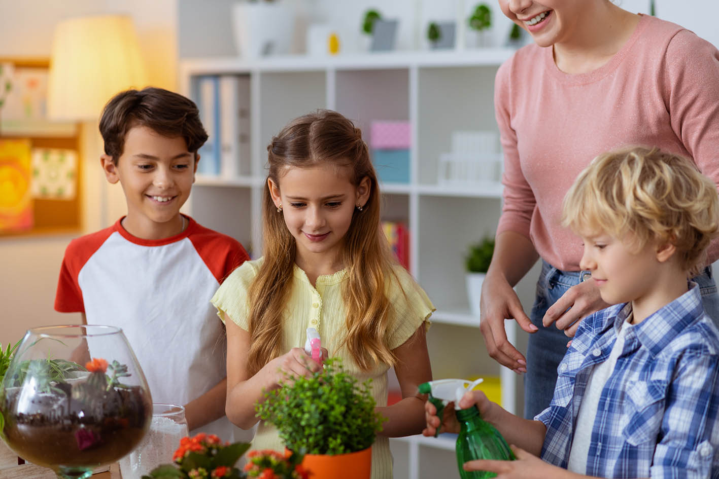 Μητέρα με παιδιά ποτίζουν γλάστρες με φυτά στο σπίτι