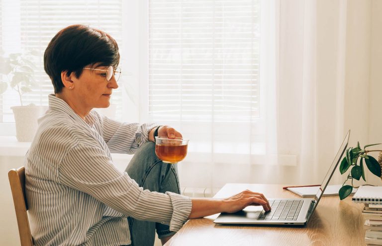 Γυναίκα μέσης ηλικίας πίνει τσάι και δουλεύει από το σπίτι