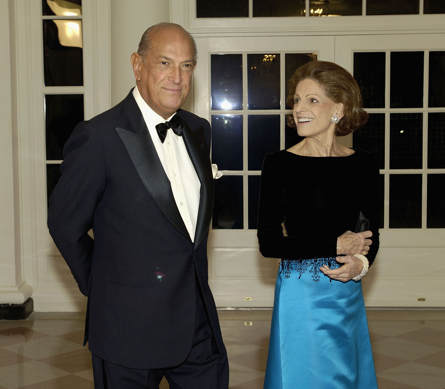 O Οscar de la Renta με τη σύζυγό του Anettte de la Renta, αντιπρόεδρο του Μητροπολιτικού Μουσείου Τέχνης, περπατούν στην αίθουσα βιβλιοπωλών στον Λευκό Οίκο καθ' οδόν προς ένα κοινωνικό δείπνο προς τιμήν του πρίγκιπα Καρόλου, πρίγκιπα της Ουαλίας, και της συζύγου του Καμίλα, στις 2 Νοεμβρίου 2005 στην Ουάσινγκτον. Το δείπνο διοργανώθηκε από τον πρόεδρο των ΗΠΑ Τζορτζ Μπους και την πρώτη κυρία.