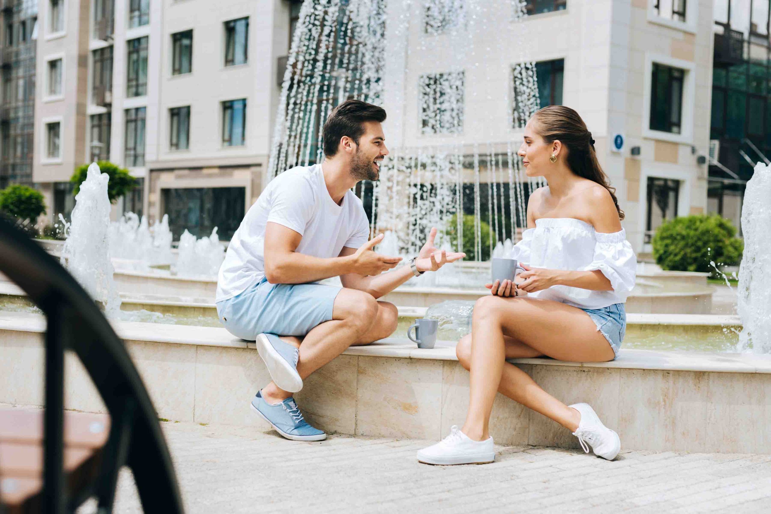 Ζευγάρι νέων στην πόλη μιλάνε πίνοντας καφέ και καθισμένοι δίπλα σε σιντριβάνι