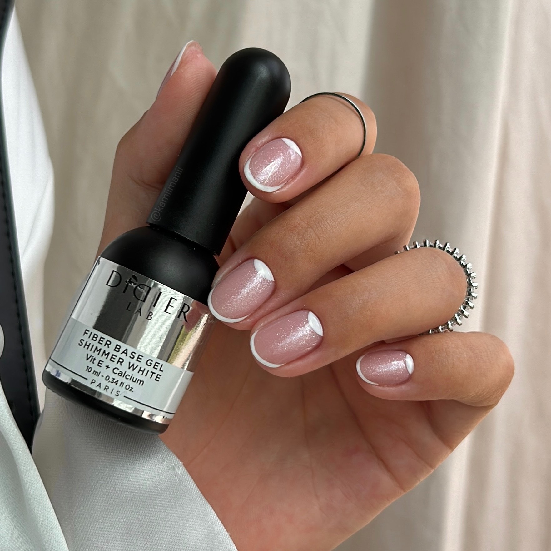 Χέρι με γαλλικό μανικιούρ που κρατάει ένα βερνίκι βάσης