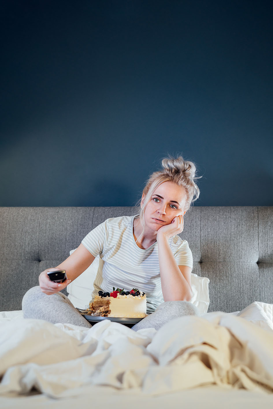 Γυναίκα στο κρεβάτι βαριέται βλέπει τηλεόραση και τρώει γλυκό