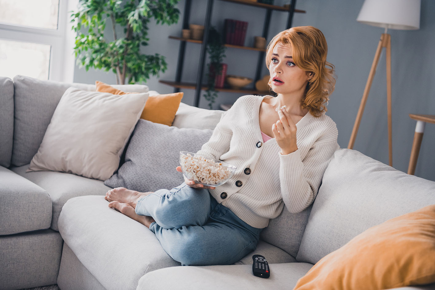 Γυναίκα στο σπίτι βλέπει τηλεόραση και τρώει σνακς