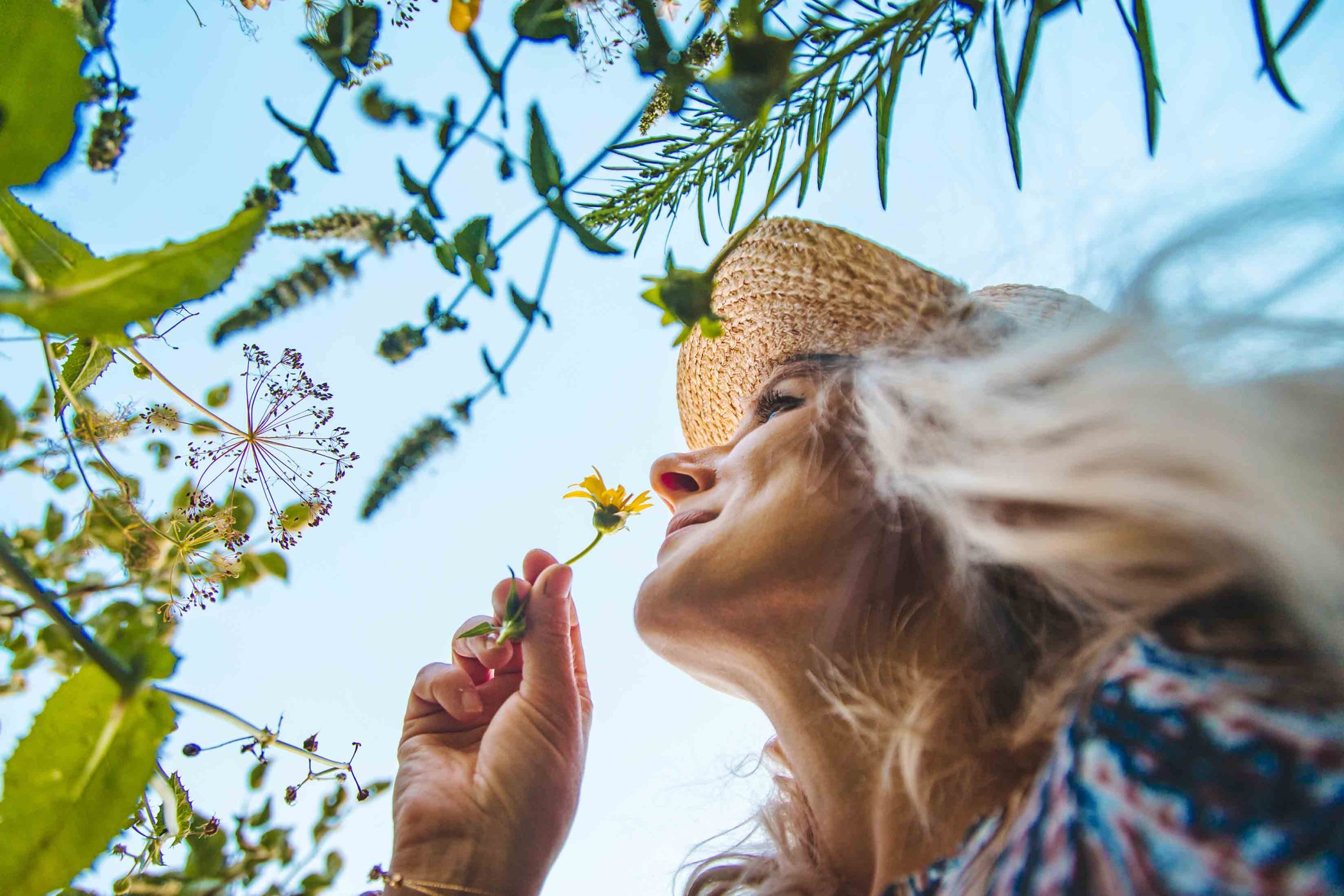 Γυναίκα με καπέλο στη φύση μυρίζει λουλούδι