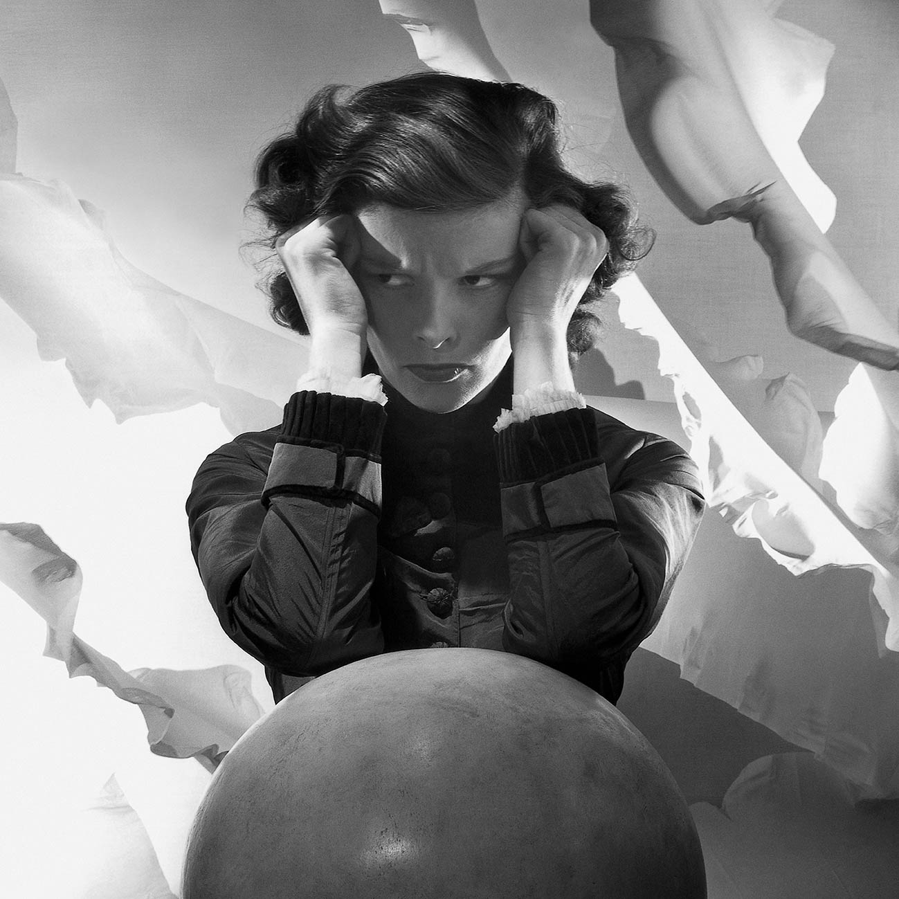 H ηθοποιός Katharine Hepburn, στέκεται με τις γροθιές της στους κροτάφους της και τους αγκώνες της να ακουμπούν σε μια μπάλα. Φωτογραφημένη από τον Cecil Beaton για το Vanity Fair 1935.