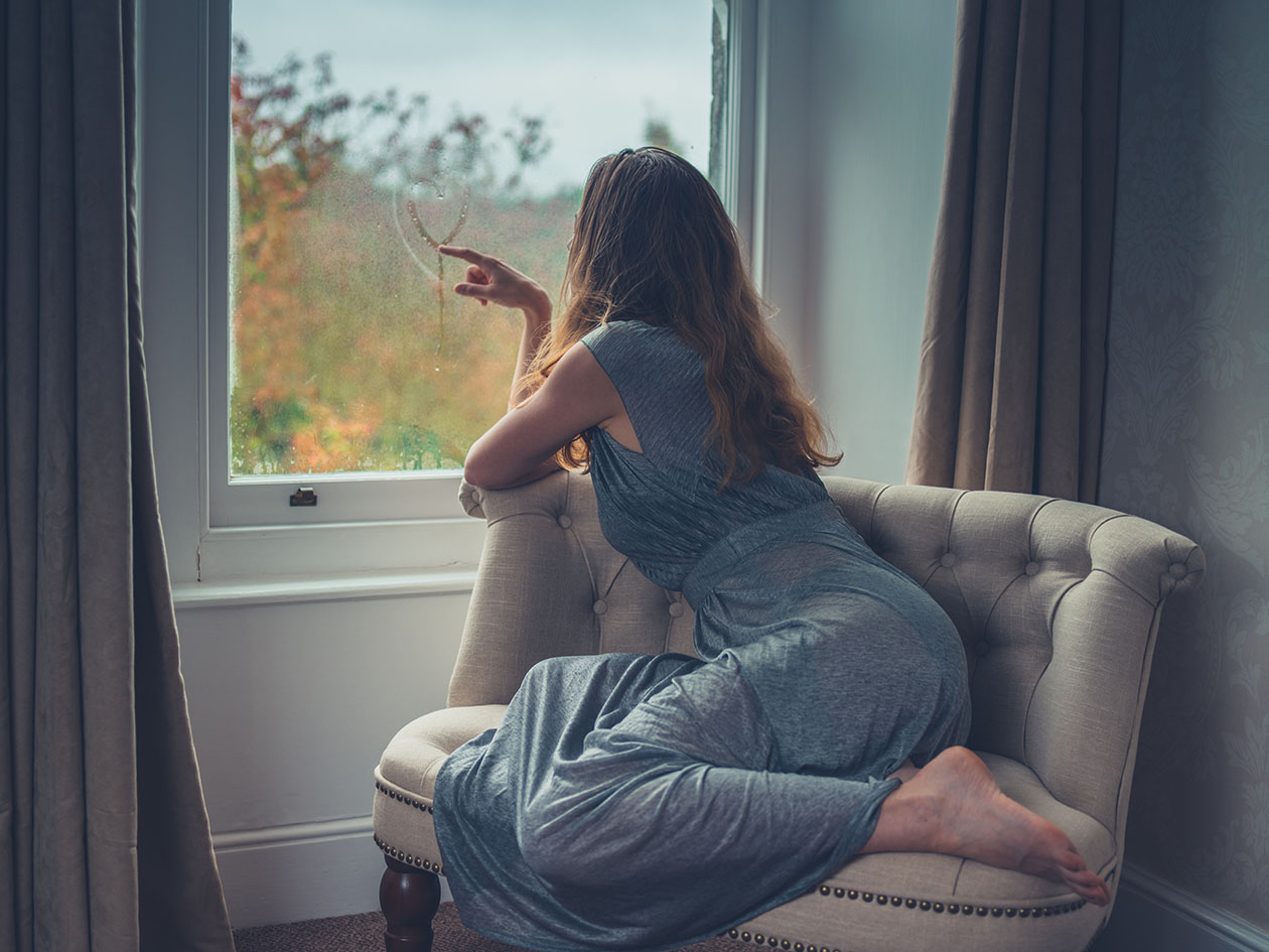 Γυναίκα σε πολυθρόνα χαζεύει από το παράθυρο