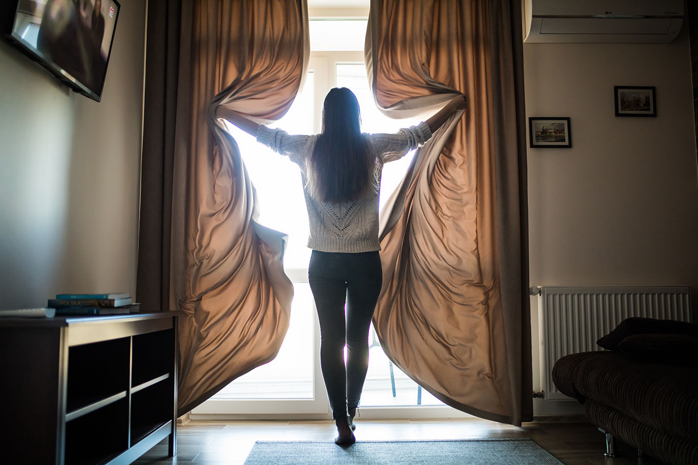 Γυναίκα ανοίγει τις κουρτίνες του δωματίου