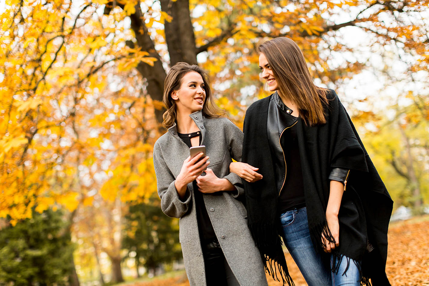 Φίλες πίνουν καφέ και περνάνε όμορφα περπατώντας σε πάρκο το φθινόπωρο