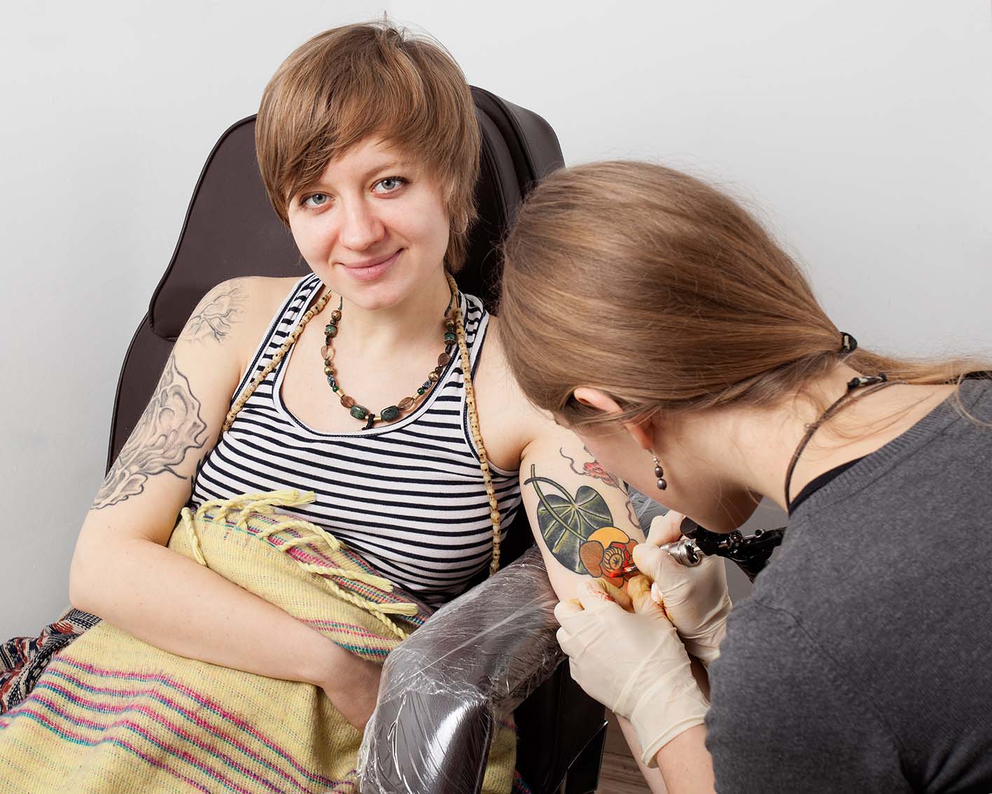 Καλλιτέχνης τατουάζ φτιάχνει ένα στο χέρι κοπέλας που χαμογελά