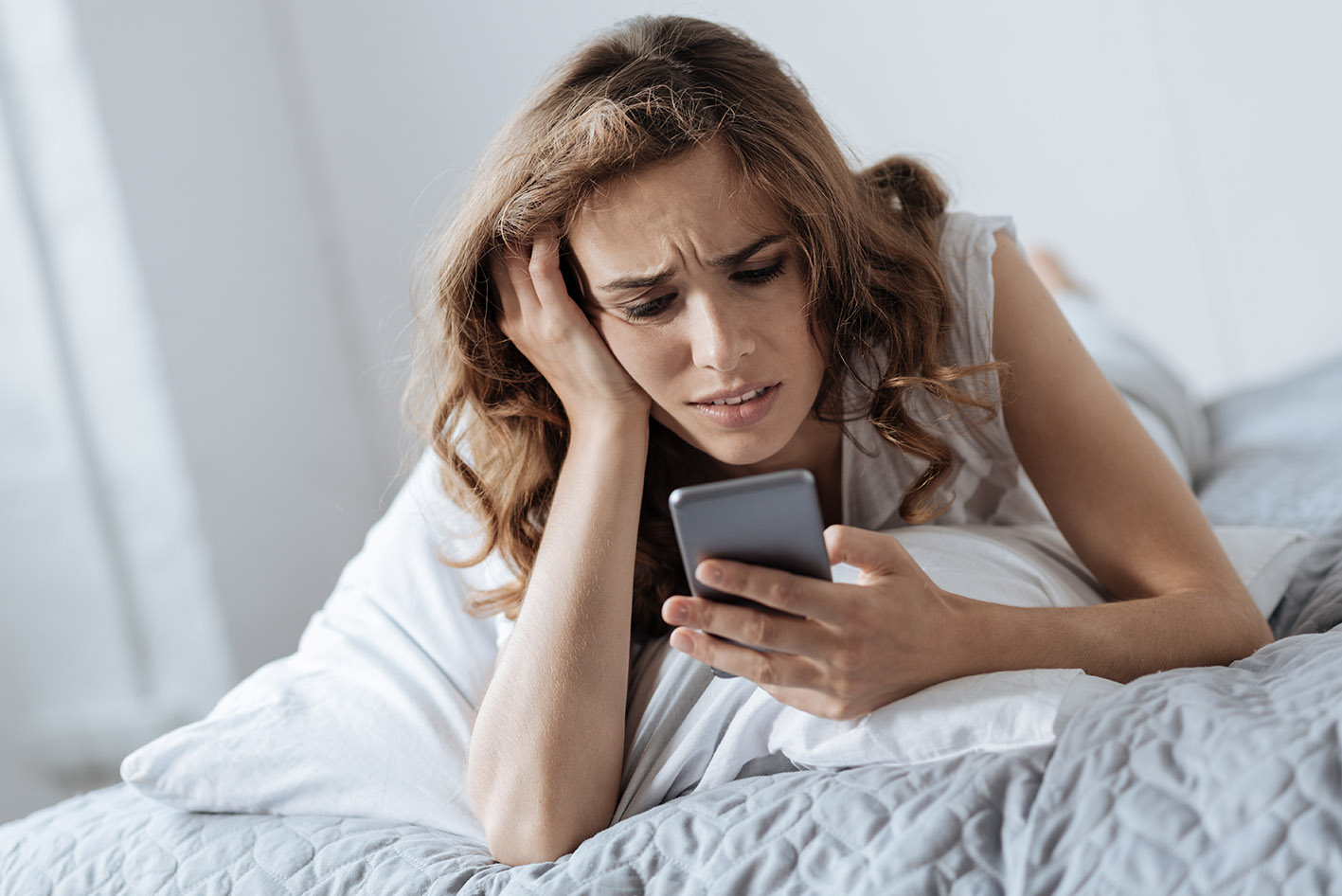 Στρεσαρισμένη γυναίκα στο κρεβάτι της βλέπει το κινητό της