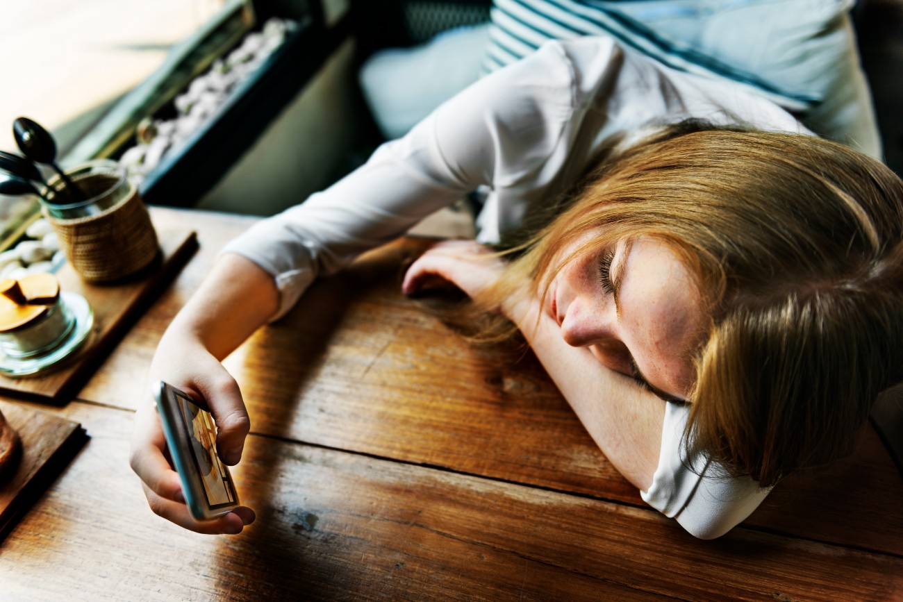 Γυναίκα στο γραφείο χωρίς ενέργεια κοιτάζει το κινητό της