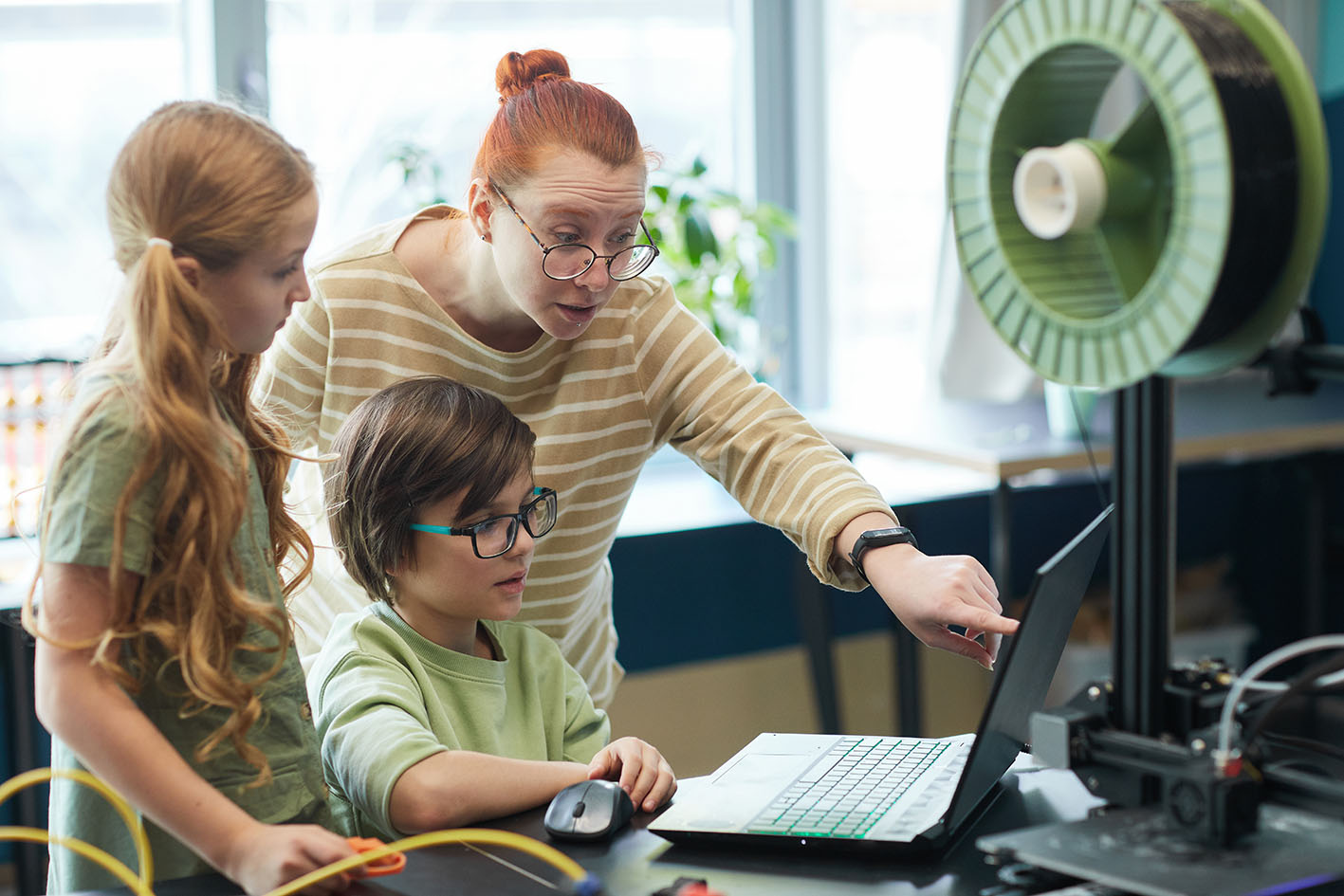 Δασκάλα και δύο μαθητές πάνω από ένα κομπιούτερ.