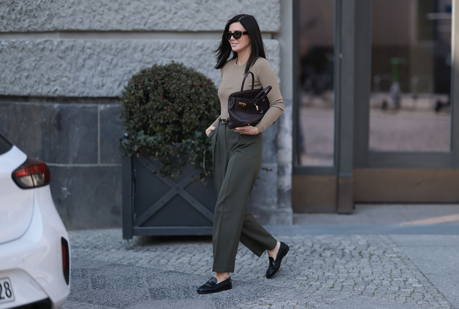 Η Leo Eberlin φορώντας oversized μαύρα γυαλιά ηλίου Yves Saint Laurent, κοσμήματα με διαμάντια Leo Mathild, εφαρμοστό, πλεκτό μακρυμάνικο πουλόβερ Arket με κλασική λαιμόκοψη σε ζεστό γκρι χρώμα, ψηλόμεσο, μακρύ, ελαφρώς φαρδύ παντελόνι Arket σε σκούρο λαδί χρώμα, μπορντό δερμάτινη ζώνη Yves Saint Laurent, κίτρινο χρυσό ρολόι Audemars Piguet, σκούρα καφέ τσάντα Birkin Hermès και μαύρα δερμάτινα μοκασίνια Chanel με γυαλιστερό φινίρισμα, στις 2 Απριλίου 2025 στο Βερολίνο της Γερμανίας.