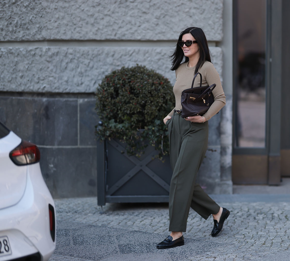 Η Leo Eberlin φορώντας oversized μαύρα γυαλιά ηλίου Yves Saint Laurent, κοσμήματα με διαμάντια Leo Mathild, εφαρμοστό, πλεκτό μακρυμάνικο πουλόβερ Arket με κλασική λαιμόκοψη σε ζεστό γκρι χρώμα, ψηλόμεσο, μακρύ, ελαφρώς φαρδύ παντελόνι Arket σε σκούρο λαδί χρώμα, μπορντό δερμάτινη ζώνη Yves Saint Laurent, κίτρινο χρυσό ρολόι Audemars Piguet, σκούρα καφέ τσάντα Birkin Hermès και μαύρα δερμάτινα μοκασίνια Chanel με γυαλιστερό φινίρισμα, στις 2 Απριλίου 2025 στο Βερολίνο της Γερμανίας.