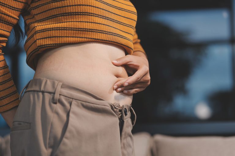 Γυναίκα πιάνει και πιέζει την κοιλιά της για να δει τα παχάκια της