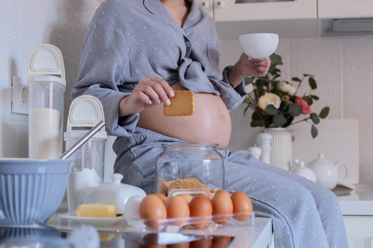 Γυναίκα έγκυος παίρνει πρωινό. Η φωτογραφία δείχνει την κοιλιά της και αβγά φλυτζάνι και φρυγανιές