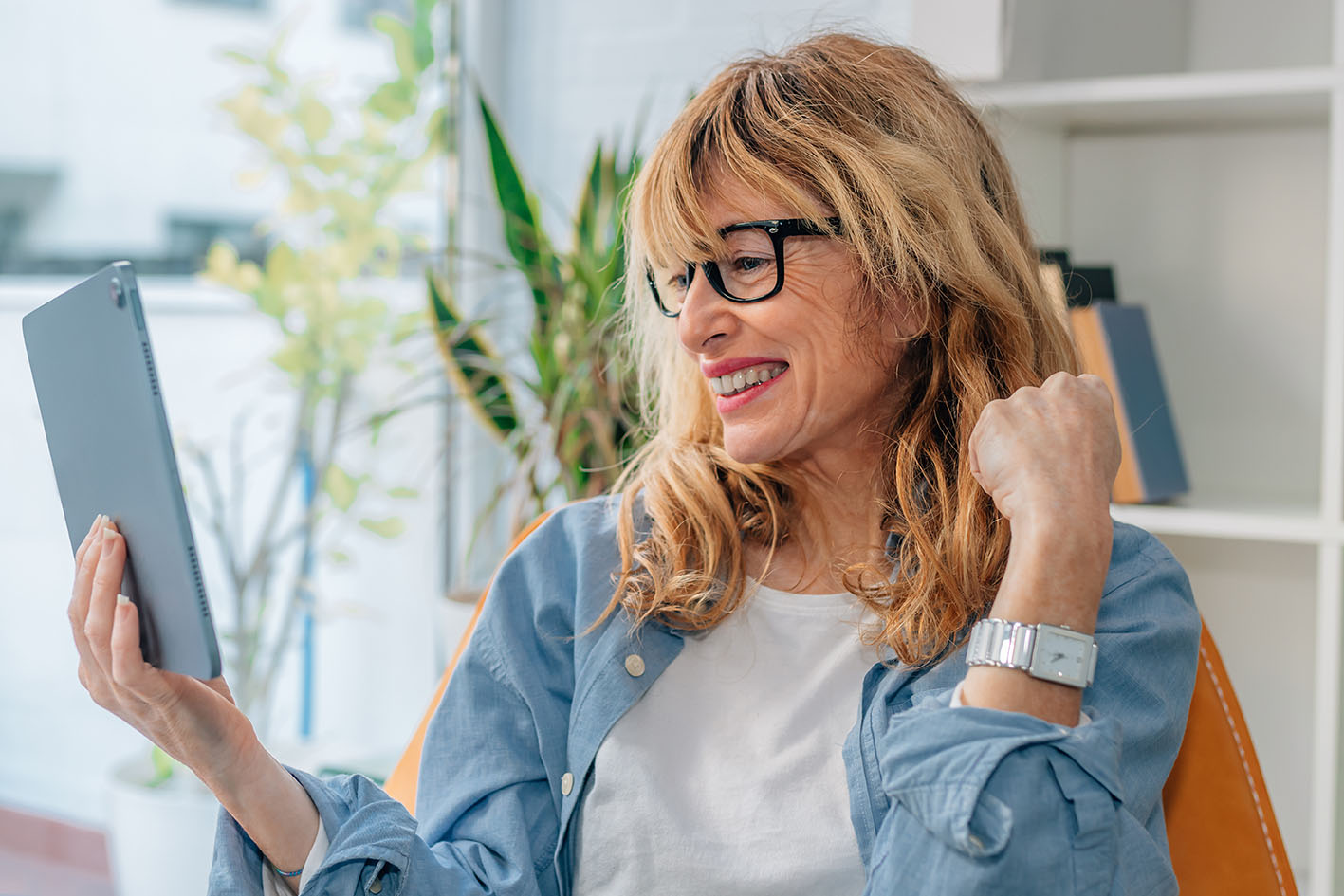 Γυναίκα μέσης ηλικίας παίζει με τα σγουρά μαλλιά της και χαζεύει χαμογελώντας το laptop της