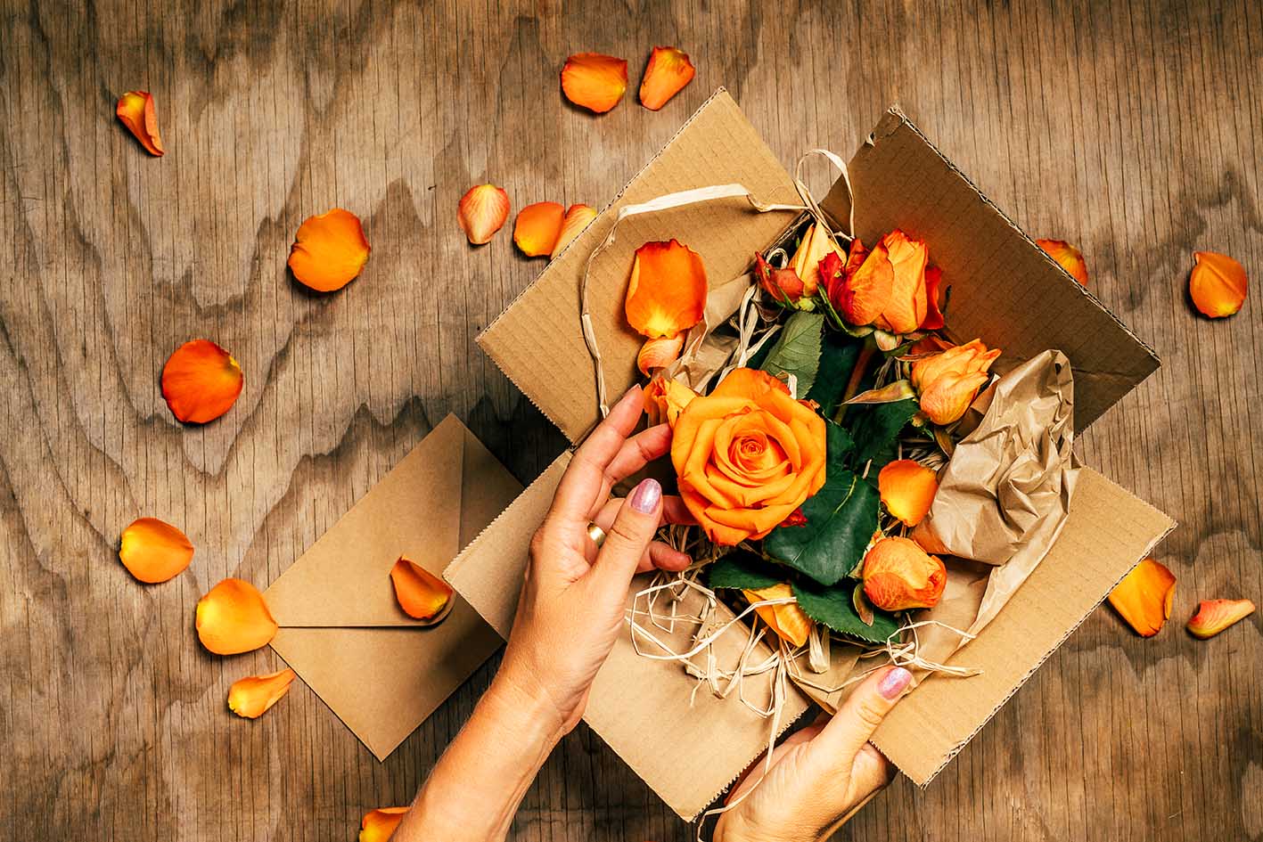 Γυναικείο χέρι σε ανοικτό κουτί που έχει μέσα λουλούδια πορτοκαλιά. Μετά τον Άγιο Βαλεντίνο ελάτε να κάνουμε ανακύκλωση.