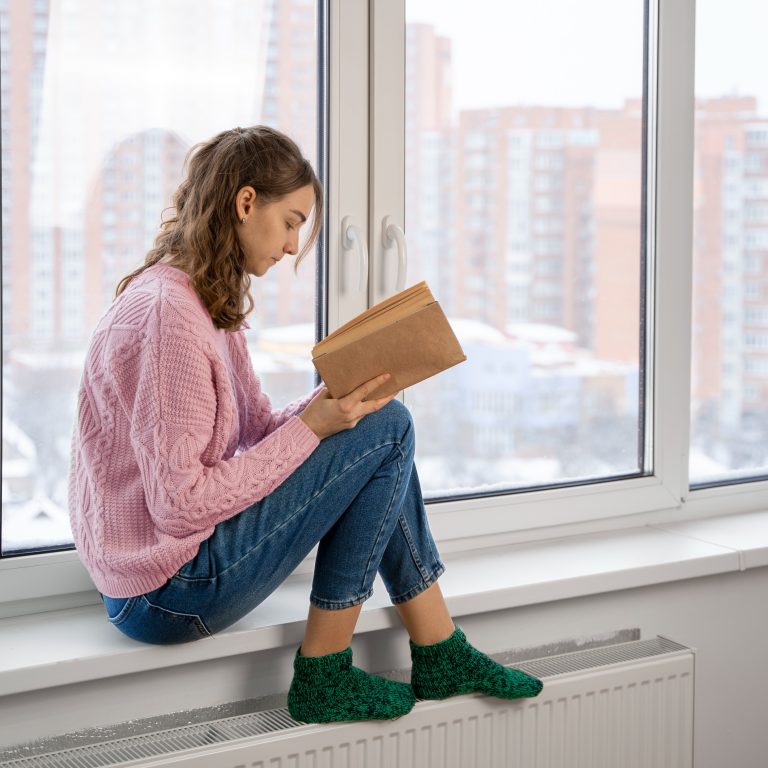 Γυναίκα διαβάζει ένα βιβλίο και ζεσταίνει τα πόδια της πάνω στο καλοριφέρ.