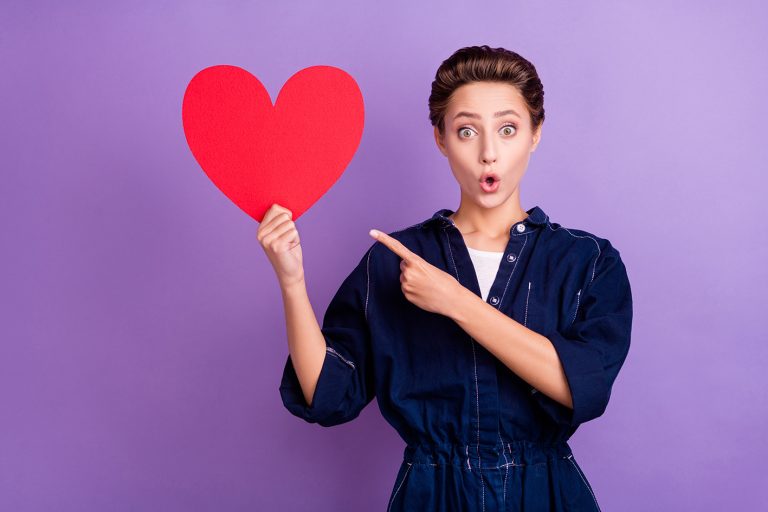 Ημέρα των ερωτευμένων και ζώδια- Αγιος Βαλεντίνος και γυναίκα δείχνει μια κόκκινη χάρτινη καρδιά που κρατά με απορία...
