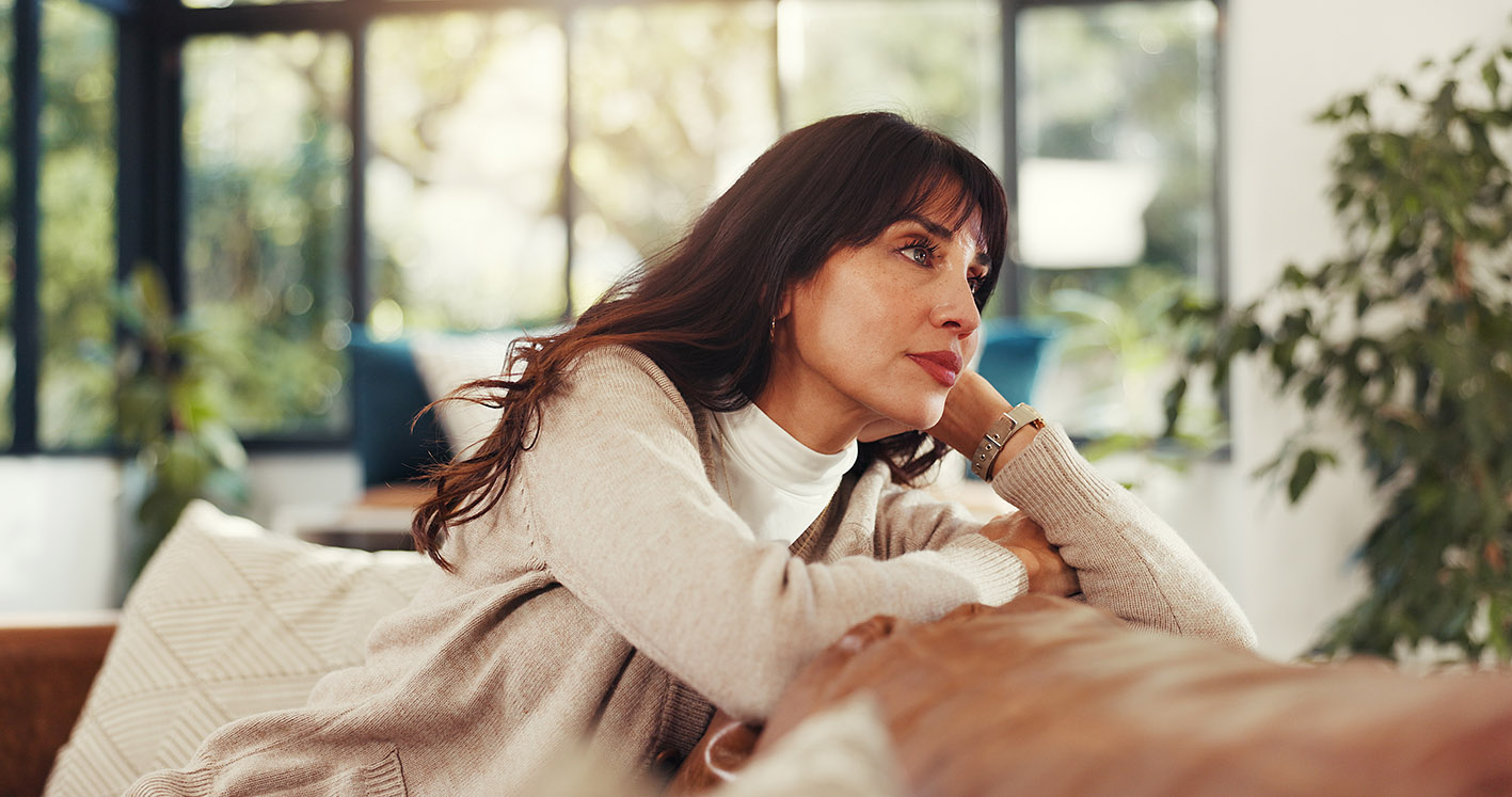 Γυναίκα μέσης ηλικίας κάθεται στον καναπέ της και ονειροπολεί.