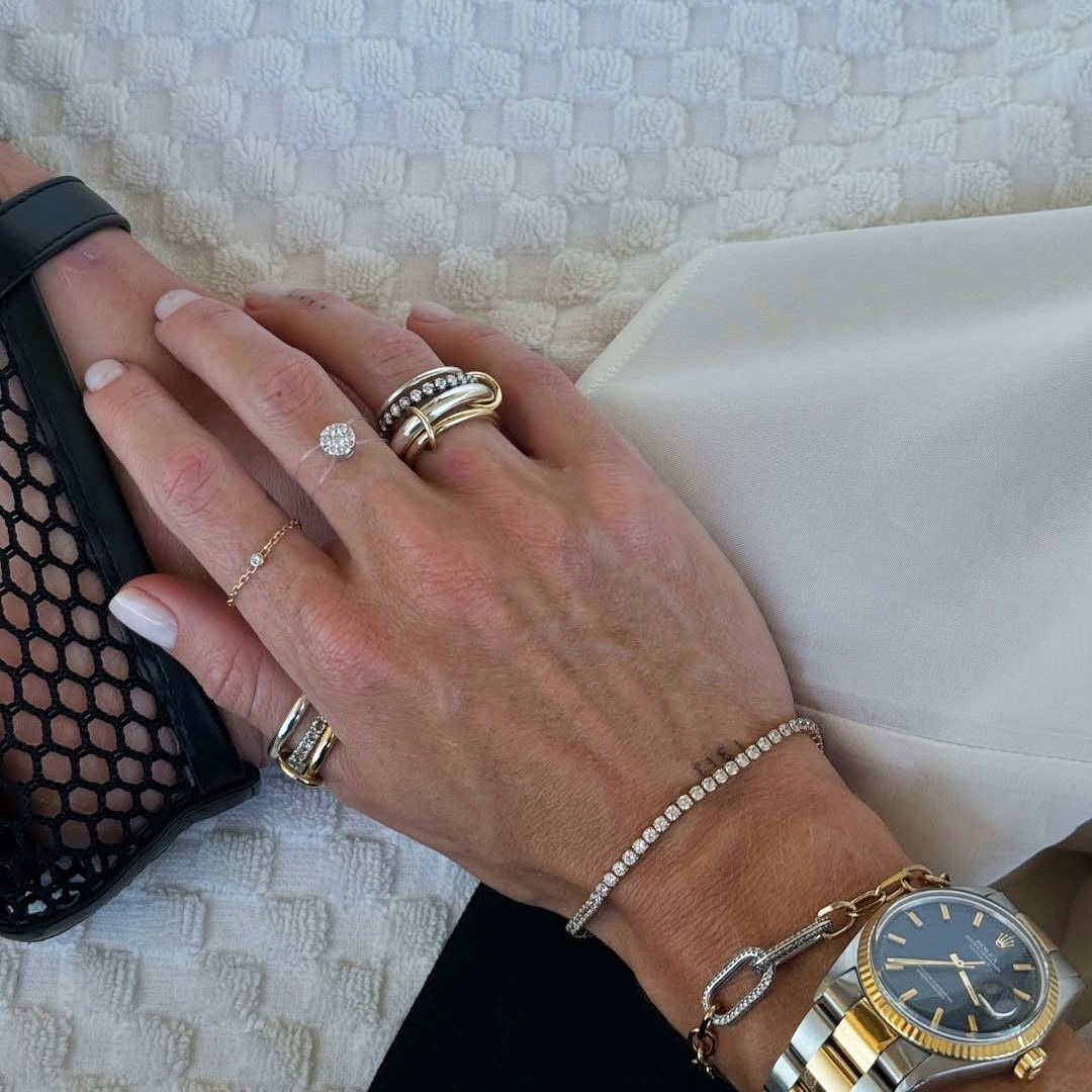 Tennis Bracelet - H νέα τάση στα κοσμήματα. Στη φωτογραφία γυναικείο χέρι με δαχτυλίδια σε σχεδόν σε κάθε δάχτυλο, μπρασελέ με διαμαντάκια και ρολόι.