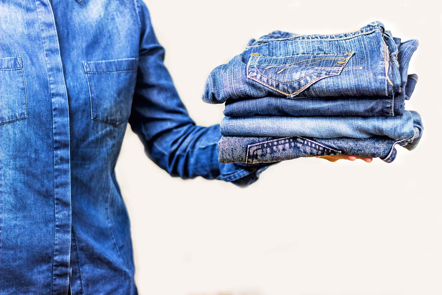 Γυναίκα κρατά ένα πάκο από διάφορα πλυμένα τζιν.