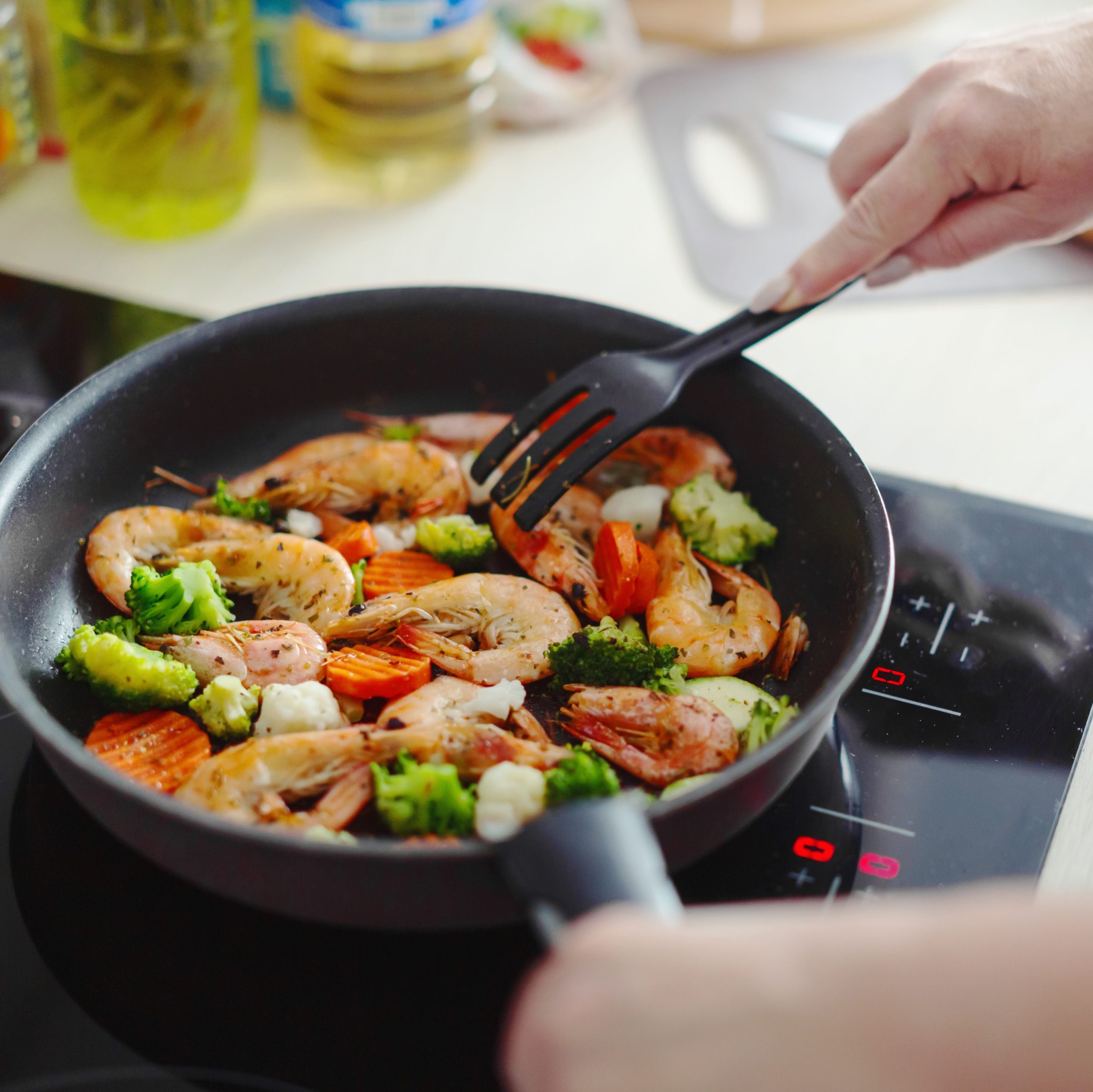 Γυναίκα μαγειρεύει σε τηγάνι λαχανικά με γαρίδες.