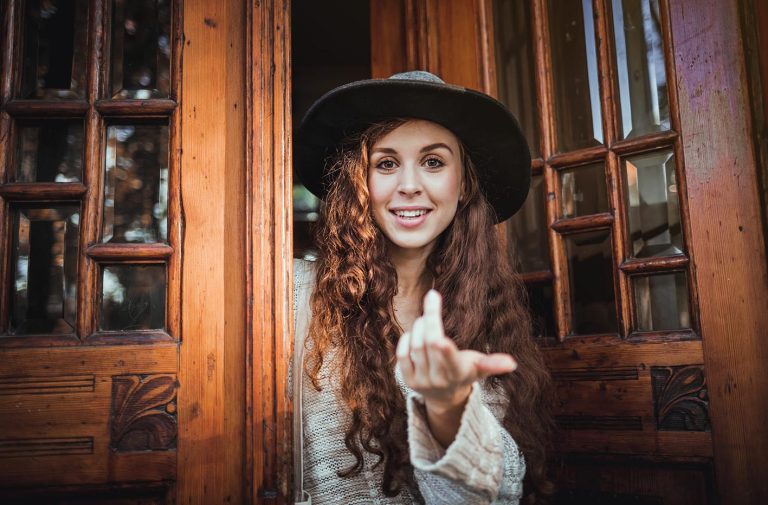 Γυναίκα κάνει σήμα να μπούμε μέσα μπροστά από ανοιχτή πόρτα.