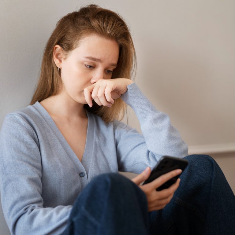 Γυναίκα κοιτάζει λυπημένη το κινητό της.