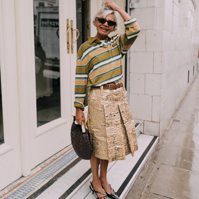 H Grece Ghanem με μεταλλική χρυσή μίντι φούστα και ριγέ πόλο μπλούζα.
