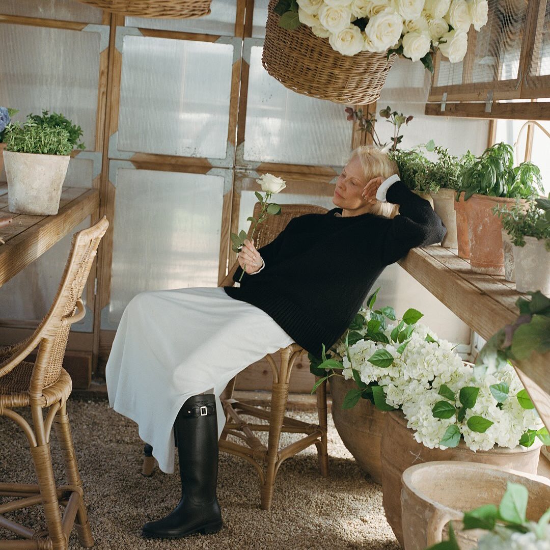 Η Pamela Anderson φοράει μπότες ιππασίας με λευκή φούστα και μαύρο πουλόβερ.