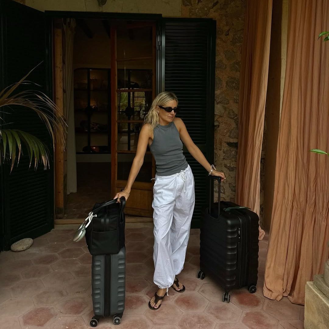 Κοπέλα με λευκό παντελόνι, γκρι τοπ και βαλίτσες.