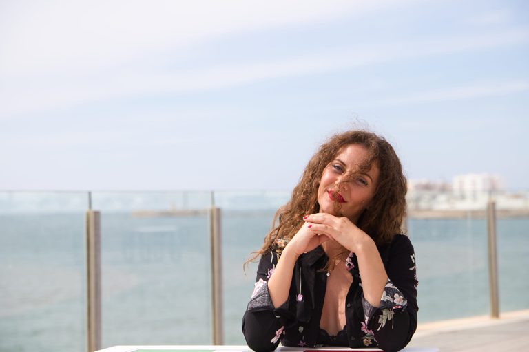 Γυναίκα μέσης ηλικίας χαμογελά. Πίσω της θάλασσα.