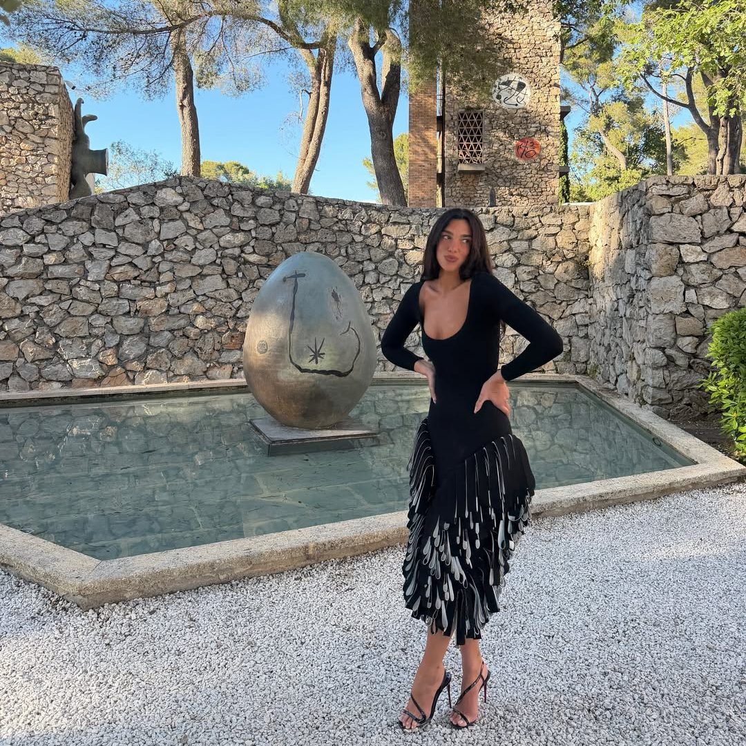 Η Dua Lipa με μαύρο μίντι φόρεμα Jacquemus με ασύμμετρο όγκο και κρόσσια στο στρίφωμα, στις Κάννες.