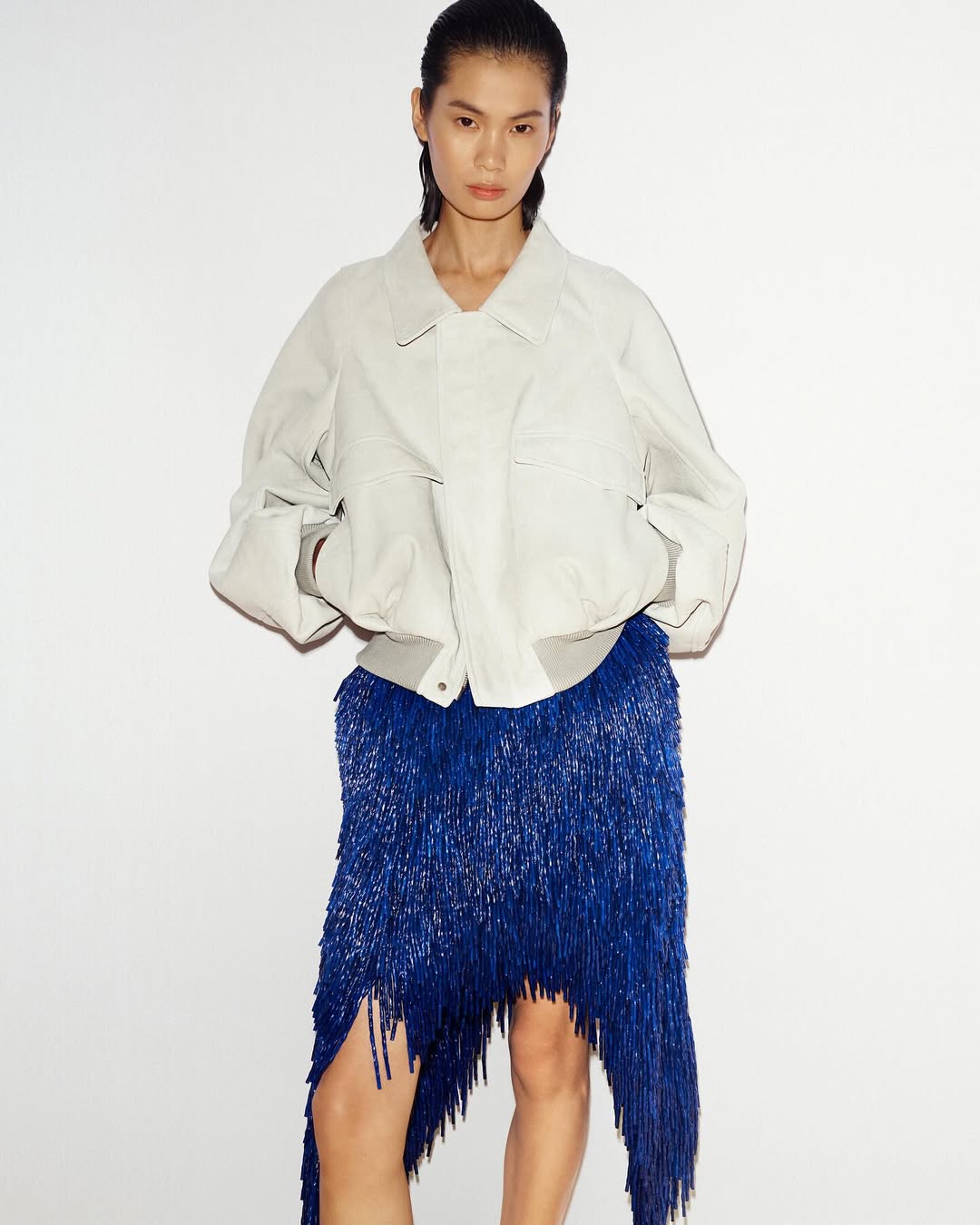 Ένα off-white τζάκετ λειτουργεί ως ο ήσυχος καμβάς για να αποθεωθεί η μπλε ηλεκτρίκ φούστα με τα άπειρα ασύμμετρα κρόσσια.