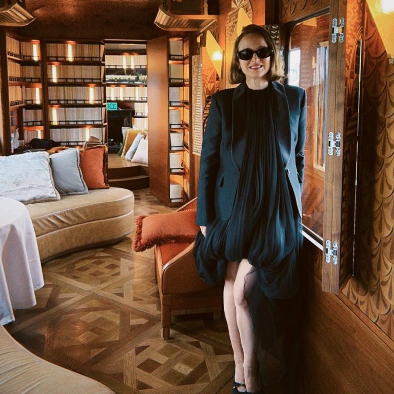 Η Natalie Portman με μαύρο μίνι balloon φόρεμα, μαύρο σακάκι και γυαλιά ηλίου, ποζάρει σε βαγόνι του Orient Express.
