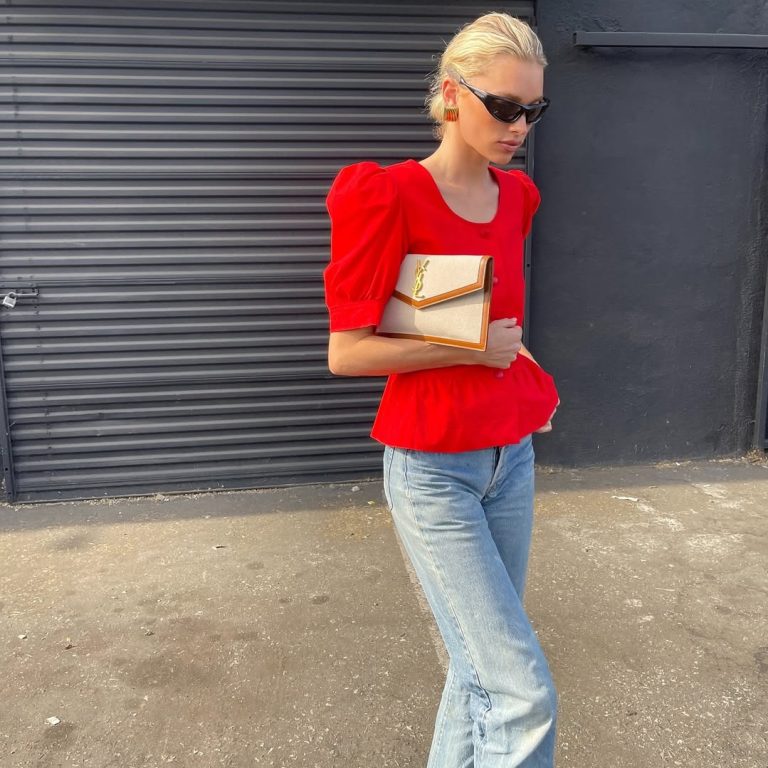 Η Elsa Hosk με έντονο κόκκινο peplum τοπ με puff μανίκια, ανοιχτόχρωμο μπλε τζιν παντελόνι και μπεζ clutch.