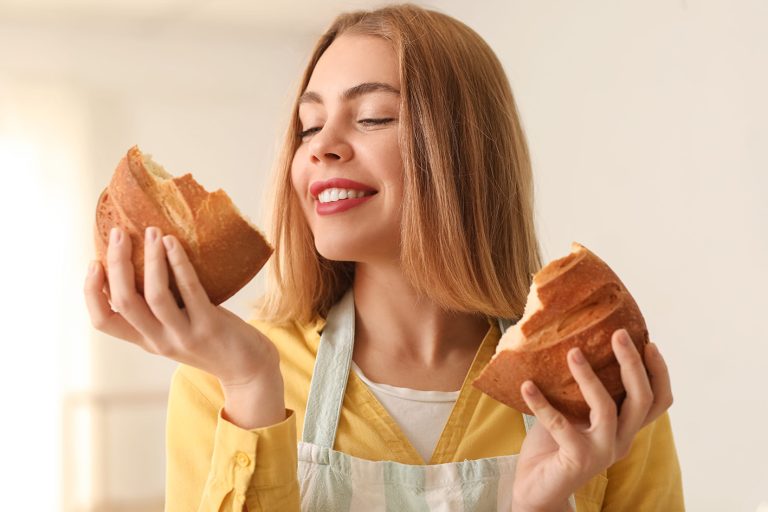 Γυναίκα μυρίζει φρεσκοψημένο ψωμί και είναι έτοιμη να το δοκιμάσει. Τελικά το ψωμί παχαίνει; Μύθοι και πραγματικότητα.