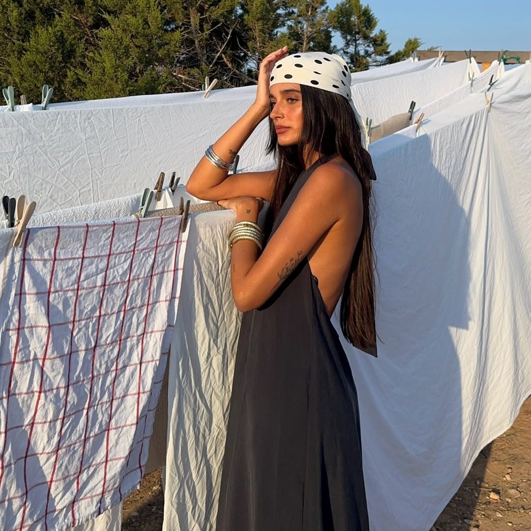 Κοπέλα με γκρι μίνιμαλ φόρεμα, μεταλλικά βραχιόλια με ακανόνιστο σχήμα και λευκή πουά μπαντάνα με μαύρες βούλες δεμένη στα μαλλιά της.