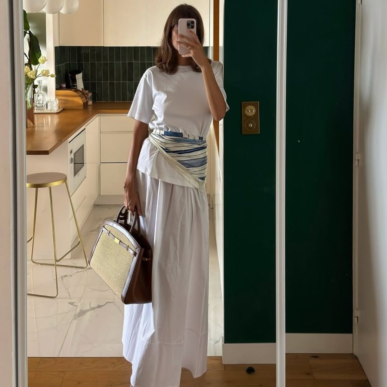 Κοπέλα με total white look με μάξι φούστα, εμπριμέ μαντήλι στη μέση, λευκά mules και υφαντή tote τσάντα με καφέ δερμάτινες λεπτομέρειες.